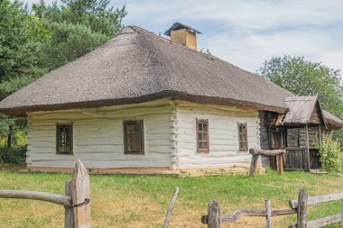 Eski bir Orta Avrupa köyünde bulunan sazdan çatılı geleneksel ahşap kulübe. Bina beyaz, ahşap kirişler, bir baca ve eski bir kuyu ve gr önünde küçük eskimiş bir çit var.