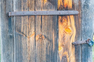 Eski bir Orta Avrupa köyünde eskimiş, dikey tahıllı ahşap kapı paslanmış menteşe ve mandal, çatlaklarla karartılmış ahşap ve yukarıdan yansıyan doğal ışık, gölgeler