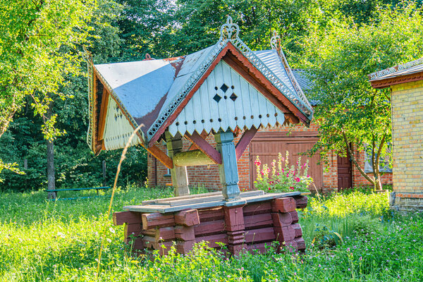Яркий красный таиландский газебо посреди пышного зеленого центральноевропейского сада, рядом со скамьей из бревен.