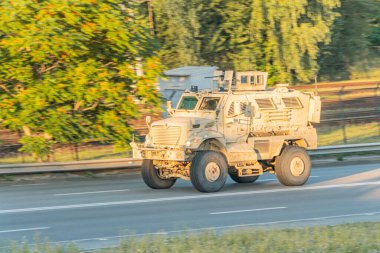 Yoldaki askeri araç, şehir ayarı, ağır tekerlekler, antenler, muhtemelen gözetleme ekipmanları, açık renk, tüm arazi, yol eğrisi, hafif ışıklandırma, sabah erken ya da geç saatlerde
