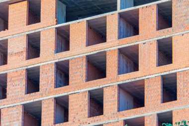 Modern bina inşaat halinde, kırmızı-turuncu tuğla duvarlar, yatay sıralar, dikey sütunlar, dikdörtgen açıklıklar potansiyel pencere veya balkonlar, beton kirişler, güçlendirilmiş yapı, farklı b