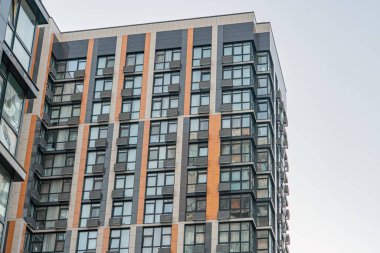 Modern, çok katlı şehir binası, dikey çizgiler, düz yüzeyler, ve açısal formlar kahverengi, bej, gri cephe koyu aksanlı, eşit aralıklı dikdörtgen pencereler, açık renk pencere kolları