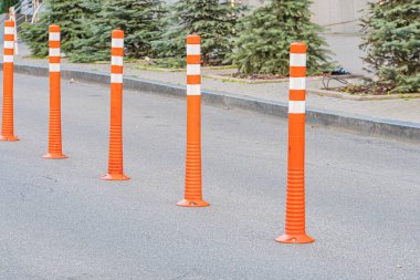Şehir yolundaki güvenlik konileri, turuncu ve beyaz şeritler, iki sıra halinde dizilmiş bir alan oluşturan şehir arka planı binalar, mağazalar, pencereler ve bitki örtüsü