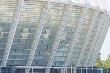 Yansıtıcı cam panelleri olan modern, kentsel yapı, bulutlu veya dağınık ışıklandırma koşulları, geometrik tasarım, çoklu seviye, metin veya markalaşma yok, gerçekçi fotoğraf tarzı