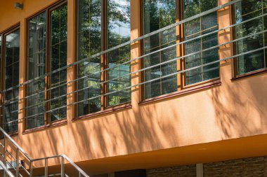 Kıvrımlı ön cepheli modern, minimalist bina, büyük pencereler, siyah mulyonlar, yatay çubuklar veya yüzgeçler, açık hava oturma alanı, yeşil merdiven, doğal gün ışığı