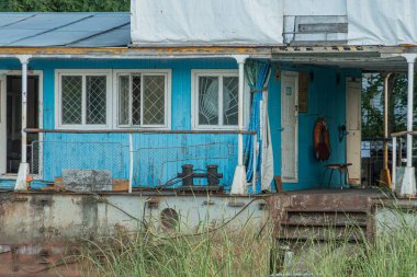 İskelede terk edilmiş mavi bir ev, konut olarak yüzen gemiler, çürüme, soyulmuş boyalar, tahta kaplı pencereler, beyaz kolonlar, paslı korkuluklar, tel örgüler, açık kapı, fazla büyümüş yabani otlar, inkar edilemez cazibe, solitu