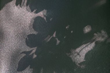 Sönük renklerde büyük bir şablonlu çiçek motifinin yer aldığı desenli kumaşın yakın görüntüsü. Işık yansımaları ve gölgeler, odaklı gerçekçi tasarım tarzının dokusunu ve derinliğini vurgular.