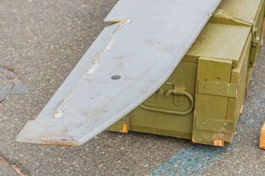 Görüntü Tanımlamasının Özeti: Büyük metalik bir uçak kanadı alüminyum veya çelik, aşınmış yeşil ve mavi bir sandık üzerinde, açık ya da kapalı bir alanda sert betondan oluşan bir zemine dayanır.