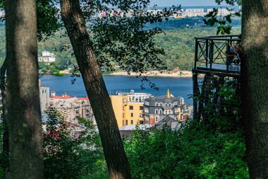 Ön planda yemyeşil bir ormanın ve arka planda bir nehirle bağlantılı iyi ışıklandırılmış bir şehir manzarasının bir manzara fotoğrafı sahne mimari tarzların bir karışımını, yükseltilmiş bir platformu ve