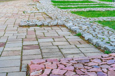Eski bir Avrupa şehrinde kavisli taş yolu, kırmızı tonlu toprak kahverengi ve gri taşlardan oluşur, düzgünce budanmış çimen alanlarını ikiye böler