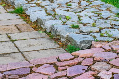 Eski bir Avrupa şehir caddesinde düzensiz kaldırım taşlarının yakın çekimi, gri, pembemsi kırmızı ve kahverengi tonlarında, bulutlu bir gün.