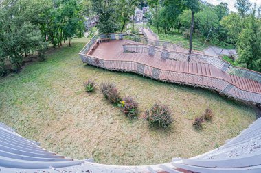 Bir parkın kuş bakışı görüntüsü, merkez yol, yemyeşil yemyeşil, simetrik taş yapılar, canlı kırmızı çatılar, merdivenler, ağaçlar, çalılar, yeşillikler, yumuşak gölgeler, sabah erken saatlerde öğleden sonra ışığı