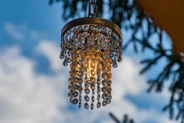 Açık hava ya da iyi ışıklandırılmış avize. Aydınlatılmış, çoklu kolları olan karmaşık tasarım. Güneş ışığını yansıtan berrak kristaller.