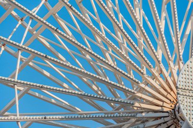 Modern bir şehir manzarasında dönme dolabı andıran özenle hazırlanmış metal bir yapıya yakın çekim. Parça karmaşık desenler, ince ışık yansımaları ve dinamik bir arayüz sergiliyor.