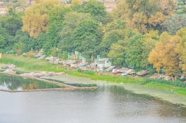 Dağınık barakaları, ahşap kalasları, dağınık tekneleri, yemyeşil ağaçları, yumuşak, uzun gölgeli gölgeleri, sıcak parıltıları olan göl yerleşiminin havadan görünüşü.