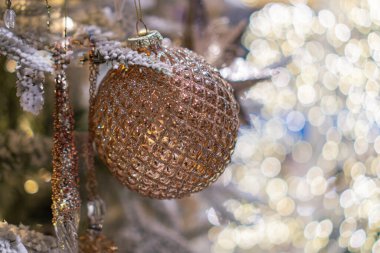 Merkezde altın, gümüş ve gül sarısı süslemelerle süslenmiş bir Noel ağacı, bir tatil ortamında bulanık ışıklarla çevrili.