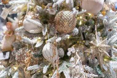 Kapalı alanda, metalik ve desenli süslemelerle süslenmiş Noel ağacı, sıcak ışıklandırma.