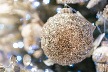 Süslü Noel ağacıyla süslenmiş, parlak süslemelerle süslenmiş, parlak altın bir küre, daha küçük süslemeler, süsler veya çelenkler ve dağınık ışıklar ile yakın çekim tatil sahnesi.