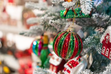 Yapay Noel ağacı, renklerle süslenmiş, öncelikle kırmızı ve yeşil, kar tanesi süslemeleri, merkezi süsleme, hafif ışıklandırma, sıcak atmosfer, kapalı ortam, bulanık sırt.