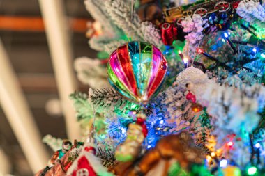 Mavi ve kırmızı balon figürü, birbirine karışmış küçük ışıklar ve beyaz kar tanesi süslemeleri de dahil olmak üzere çeşitli süslemelerle dolu renkli bir Noel ağacının yakın görüntüsü