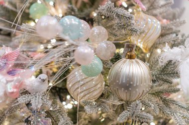 Pastel süsler ve boncuklu çelenklerle dekore edilmiş bir Noel ağacı, sıcak ortam ışıkları altında.