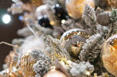 Noel ağacının çok renkli süslemeleri ile yakın plan, ağırlıklı olarak altın, gümüş ve mavi kümeler, dallar arasında kaynaşmış küçük küreler, sıcak ve davetkar ışık kalıpları.