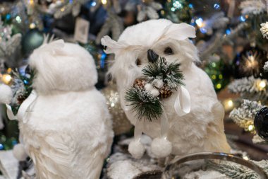 İki beyaz baykuş süslenmiş bir Noel ağacının dalında oturur, neşeli ışıklar ve çam kozalaklarıyla rahat bir tatil atmosferi, yumuşak gölgeler, sıcak renkler ve tuhaf bir tarzı vardır.