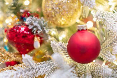 Belirgin bir şekilde yerleştirilmiş bir Noel ağacı, parlak kırmızı ve altın süslemelerle süslenmiş, sıcak ışık altında bulanık bir odada.