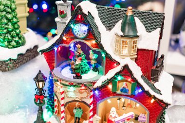 Bir Noel köyü sahnesinde şenlikli dekorları, yeşil çelenkleri, açık pencereleri ve bacası olan kırmızı çatılı bir ev Noel Baba figürü ve ren geyiği Kyiv, Ukrayna - 12 Kasım 2025