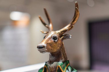 Metalik bir geyik heykelinin, muhtemelen Ukrayna 'nın başkenti Kyiv' de 12 Kasım 2025 'te kurulmuş bir ev veya mağazada bulanık bir arkaplan karşısında yeşil aksanlı olması muhtemel.