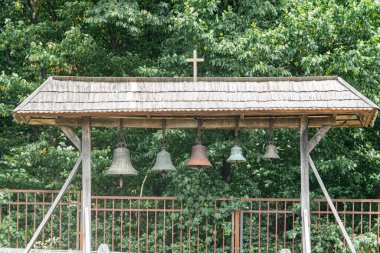 Eski Orta Avrupa köyü üç metal çan, yemyeşil arka plan, parlak ışıklandırma, natüralist tarz, zemin katmanlı perspektif ile Rustik ahşap pavyon kuruyor