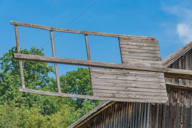 Eski ahşap köy binası, yel değirmeni, yıpranmış kiremitler, hafif hareket eden yelkenler berrak mavi gökyüzü, canlı ahşap dokular