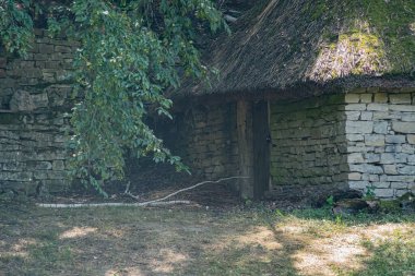 Orta Avrupa 'da çimen ve yapraklarla çevrili taştan bir ahır. Gündüz vakti doğal aydınlatma. Toprak, soluk renk paletleri, yeşiller.