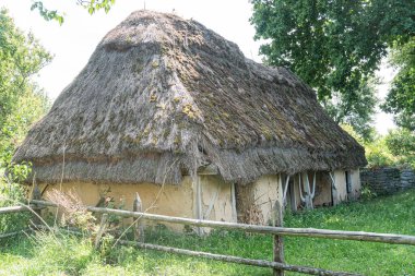Orta Avrupa 'nın ücra bir köyündeki sazdan yapılmış, samandan ya da sazlıktan yapılmış konik bir çatısı olan eski bir kır evi. Sahne çimenli alanlar, düşük bitki örtüsü ve doğal toprak tonlarını içeren bir bahçeden oluşuyor.