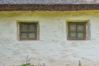 Siyah sazdan çatılı ve iki pencereli yıpranmış, taş veya alçı bir yapının yakın görüntüsü Nötr renk paleti, durağan sahne