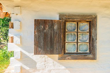 Yıpranmış, beyaz duvarlı, penceresi ve kepenkleri olan bir Orta Avrupa binası, kırsal bir köyde, aydınlık altında. Yapı yaş ve doğal kahramanlık belirtileri gösteriyor.