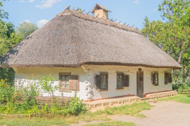 Kırsal Orta Avrupa köyü Thatched çatı konik ev, muhtemelen taş veya sıva duvarlar, koyu ahşap kirişler, kepenkli çoklu pencereli cephe, küçük bahçe alanı, çimenli zemin, c ile mavi gökyüzü