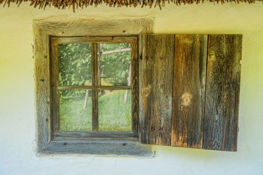 Beyaz duvarlı Orta Avrupa binasındaki eski kırsal pencere sazdan çatılı, yaş ve hayvan derisi belirtileri gösteren iç görünümü kapsayan başka bir pencere örtüsü ve açık gökyüzü ortaya çıkardı