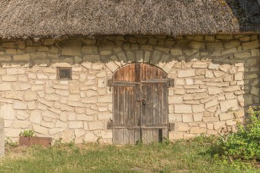 Eski bir Orta Avrupa köyünde kemerli kapı aralığı olan taştan bir bina. Çatılı, dokulu taş cephe, ahşap kapı, toprak renkler, doğal aydınlatma ve yeşillik.