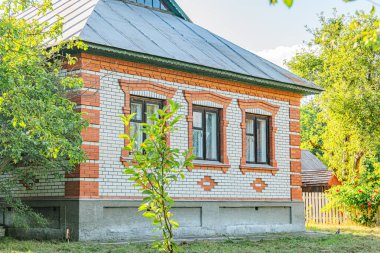 Kırmızı ve beyaz geleneksel Orta Avrupa kır evi birden fazla penceresi, yeşilimsi mavi çatı kiremitleri, yakınındaki ağaçlar, açık mavi gökyüzü, parlak ışık