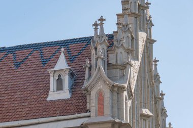 Karmaşık taş işleri, sivri kemerler, ayrıntılı oymalar, kırmızı kiremitli çatı ve taretlerle dolu eski Gotik Roma Katolik kilisesi, mimari ayrıntıları vurguluyor.