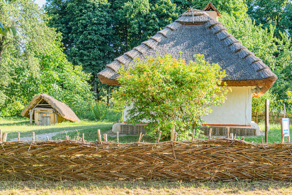 Деревенский сад Древней Центральной Европы с деревенским забором, соломенной крышей и пышной зеленью под облачным небом