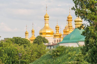 Çok sayıda altın kubbeli binaları olan büyük bir dini kompleks ve yeşil ve açık gökyüzü ile çevrili daha küçük yeşil çatılı bir bina.