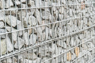 Eski bir Avrupa şehrinde, metal şebeke ile örülmüş, taş bir duvara yakın çekim, sessiz toprak tonları, dokulu gölgeler, açılı perspektif.