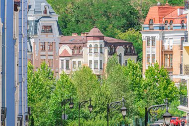 Eski bir Avrupa şehrinde, kanyon benzeri binalar, çeşitli mimari unsurlar, sütunlar, dekoratif cepheler, koyu griler için nötr renk palet ışığı, yemyeşil ağaçlar...