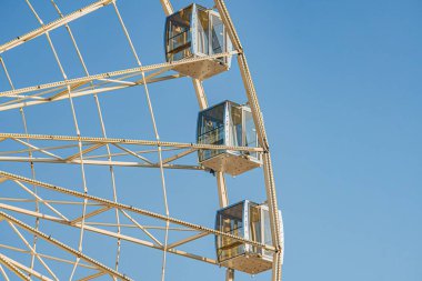 Açık mavi bir gökyüzünün altında parlak sarı ve beyaz dönme dolap şehir ortamında, boş kompartımanlar, birçok telli büyük yapı, doğal zıt alan arka planı, doğrudan aydınlatma, gölge yok.