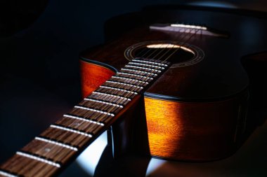 Koyu renkli, parlak bir akustik gitarın yakın plan çekimi, görünür ahşap tahıllı, boyun ve başlığa odaklanmış, fretboard boyunca altı çift olarak düzenlenmiş, sicimler merkez dışı bir başlığa yol açar.