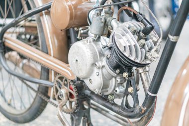 Eski motosiklet motorunun bulanık arka planda yakın plan görüntüsü, yumuşak ışıklandırma ve doku ve detaylara odaklanma ile eski metalik parçaların sessiz tonlarda sergilenmesi