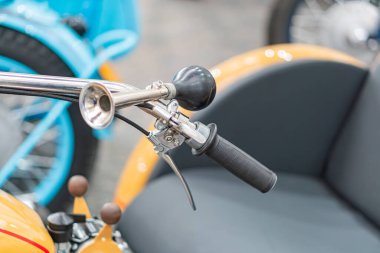 Motosiklet gidonu ve koltuğunun yakın plan görüntüsü, kapalı alanda ışıklandırma, monte göstergesi, gaz tutuşu, fren kolu, arka planda birden fazla motosiklet