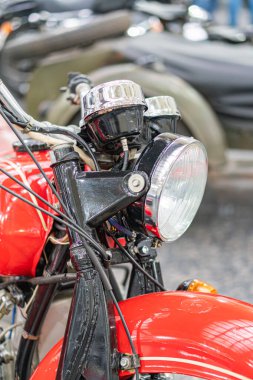 Muhtemelen 20. yüzyılın ortalarından kalma, eski tarz far, görünür göstergeler ve berraklık ve deliğe odaklanan eski model gerçekçi araçların toplandığı bir yerde sergilenen klasik kırmızı ve siyah motosiklet.